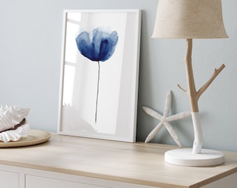 Könnte beinhalten: Eine weiße Kommode mit einer hellbraunen Oberseite und einer Schublade. Eine weiße Lampe mit einem natürlichen Astsockel und einem beigefarbenen Leinenlampenschirm steht auf der Kommode. Ein gerahmtes Aquarellbild einer blauen Blume befindet sich auf der Kommode links von der Lampe. Eine weiße Muschel und ein Seestern liegen auf der Kommode.