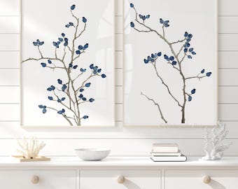 May include: Two framed watercolor prints featuring branches with blue berries. The artwork has a minimalist style with a neutral color palette. The frames are a light beige color, and the background is white.
