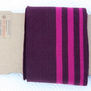 Può includere: Polso in maglia bordeaux con due strisce rosa. Il polsino ha un'etichetta che recita "OEKO-TEX® STANDARD 100", a indicare che il tessuto è certificato privo di sostanze nocive.