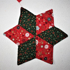 Peut inclure: Un dessous de plat matelassé en forme d'étoile rouge et verte avec un motif sur le thème de Noël. Le dessous de plat est fait de tissu avec une variété de petites étoiles, de flocons de neige et d'ornements.