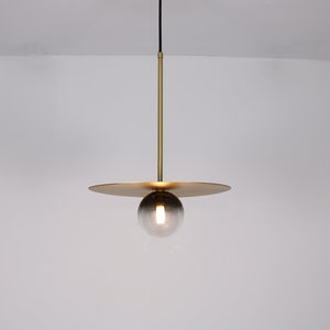 May include: A gold pendant light with a round, smoked glass shade and a flat, circular canopy.