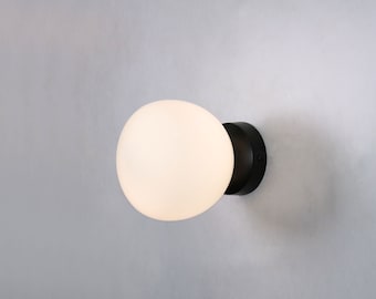 May include: A modern wall sconce featuring a round, frosted glass globe light fixture. The light is mounted on a dark, circular base. The text "Glossy square glass ø12" is visible.