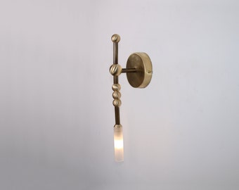 May include: A brass wall sconce with a frosted glass shade and a unique, geometric design. The sconce has a round base and a long, thin arm with a series of small, round beads.