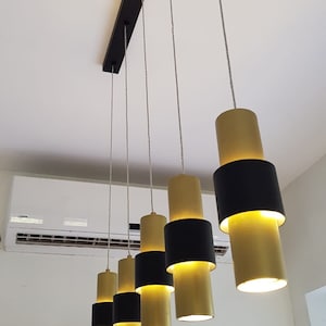 May include: A set of six gold and black pendant lights hanging from a black metal track. The lights are cylindrical in shape and have a modern design.