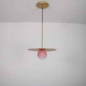 May include: A modern pendant light fixture with a gold finish and a pink glass globe. The globe has a white gradient at the bottom.