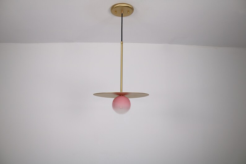May include: A modern pendant light fixture with a gold finish and a pink glass globe. The globe has a white gradient at the bottom.