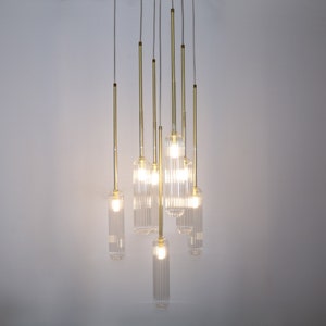 May include: A modern chandelier with eight clear glass pendant lights hanging from a ceiling. The lights are suspended from thin gold metal rods.