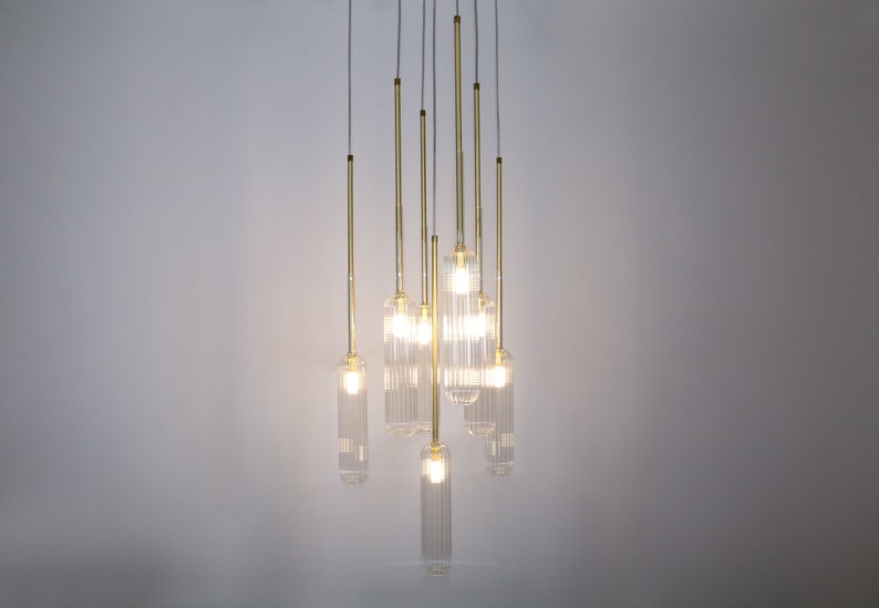 May include: A modern chandelier with eight clear glass pendant lights hanging from a ceiling. The lights are suspended from thin gold metal rods.