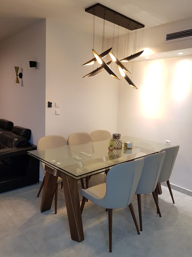 May include: A glass dining table with a wooden base and six beige chairs. The table has a modern design with a clear glass top and a sleek wooden frame. A modern light fixture hangs above the table, adding a touch of contemporary style to the dining room.