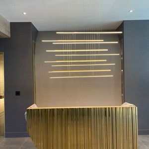 May include: A gold-colored reception desk with vertical grooves, illuminated by a modern light fixture with multiple horizontal bars.