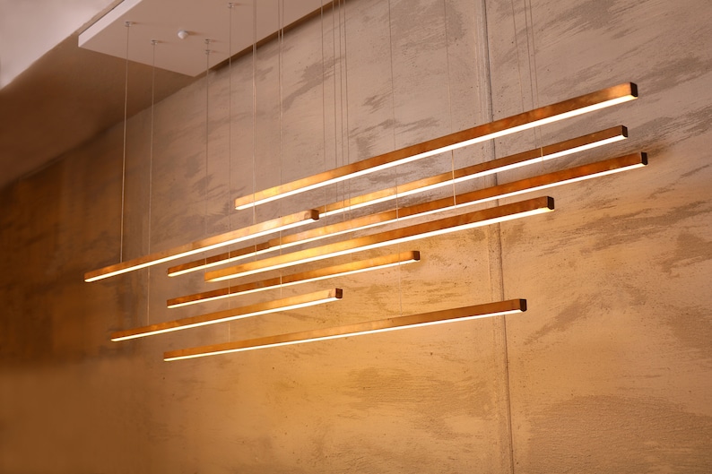 May include: A modern light fixture with multiple gold-toned rectangular bars hanging from the ceiling. The bars are arranged in a staggered pattern, creating a geometric design.