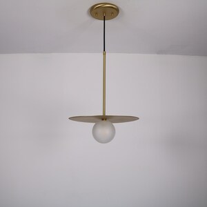 May include: A gold pendant light with a frosted glass orb and a flat, circular shade.
