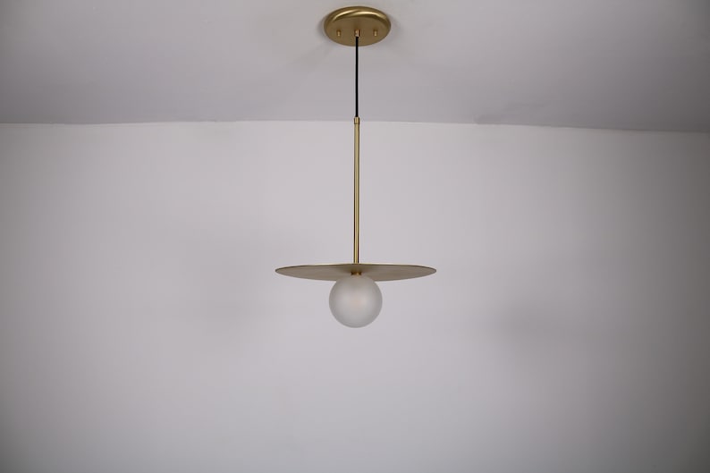 May include: A gold pendant light with a frosted glass orb and a flat, circular shade.
