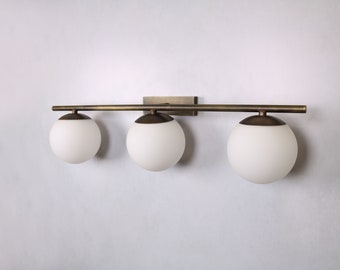 May include: A three-light vanity light fixture with a brushed brass finish and white glass globes.