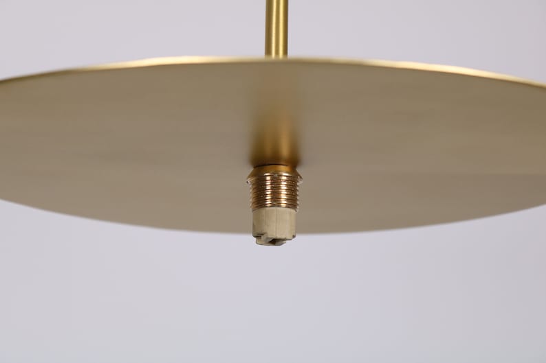 May include: Close-up of a gold-colored ceiling fixture with a round, flat canopy and a threaded brass socket.