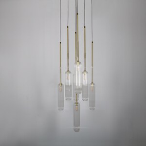 May include: A modern chandelier with seven clear glass cylinders hanging from a white ceiling. Each cylinder has a gold metal rod and a light bulb inside.