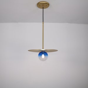 May include: A gold pendant light with a blue and white glass globe. The light fixture has a flat, circular canopy and a thin, gold rod.