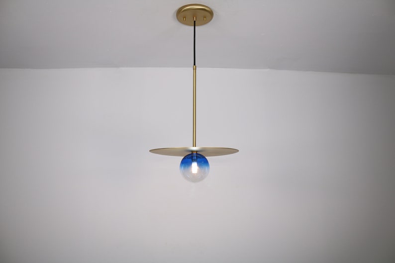 May include: A gold pendant light with a blue and white glass globe. The light fixture has a flat, circular canopy and a thin, gold rod.