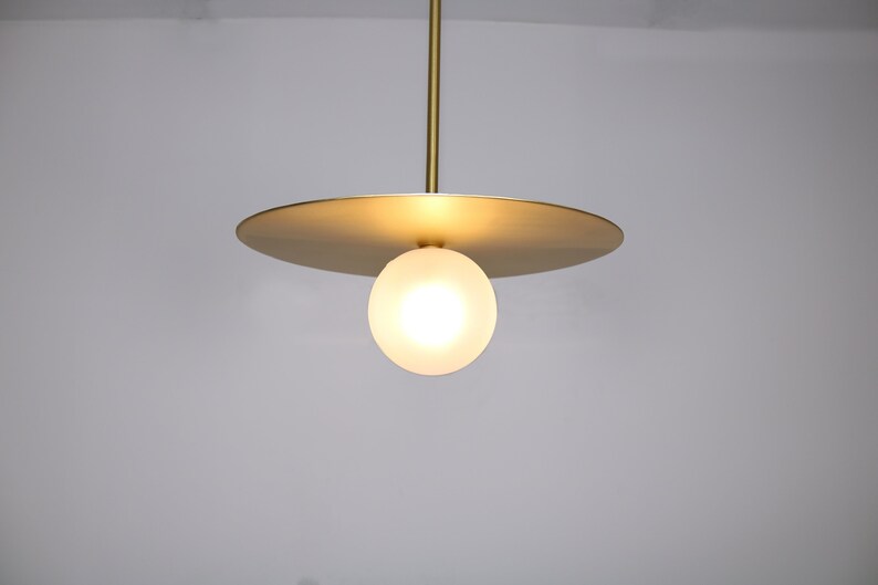 May include: A gold pendant light fixture with a round, frosted glass globe and a flat, circular metal shade.