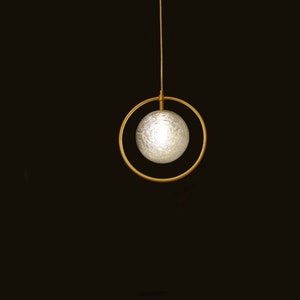 May include: A modern pendant light fixture with a white frosted glass orb suspended within a gold metal ring.