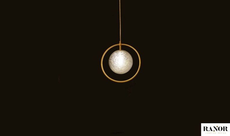 May include: A modern pendant light fixture with a white frosted glass orb suspended within a gold metal ring.