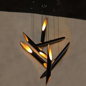 May include: A modern black and gold pendant light fixture with multiple long, thin, cylindrical shades. The shades are angled in different directions, creating a dynamic and geometric design.