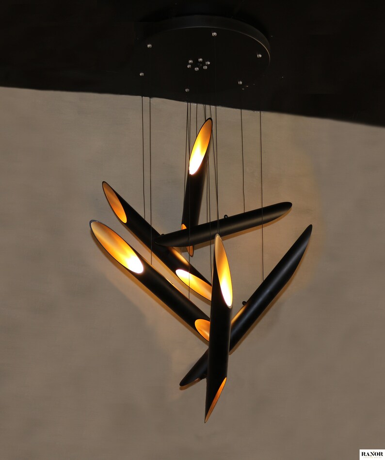 May include: A modern black and gold pendant light fixture with multiple long, thin, cylindrical shades. The shades are angled in different directions, creating a dynamic and geometric design.