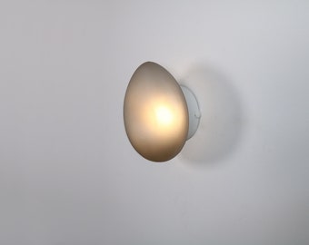 May include: A white wall mounted light fixture with a frosted glass shade in the shape of an egg. The light is on and illuminating the room.