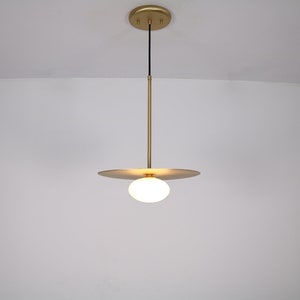 May include: A gold pendant light with a white globe shade and a thin, flat, circular plate.