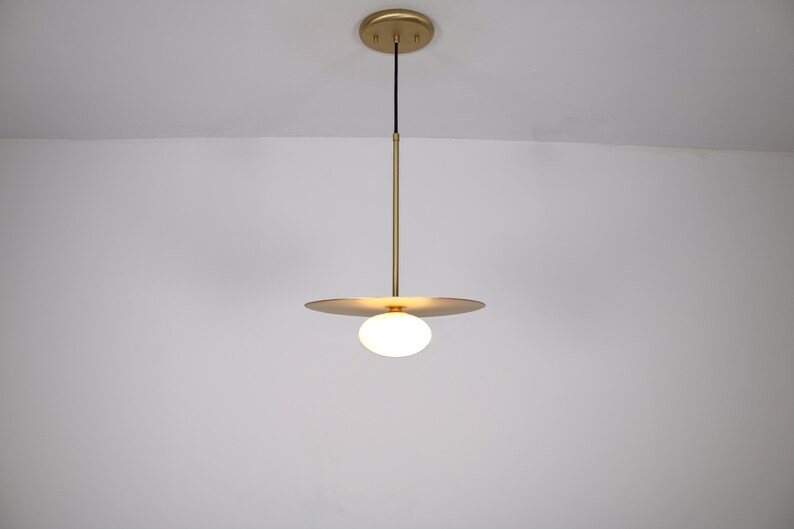 May include: A gold pendant light with a white globe shade and a thin, flat, circular plate.