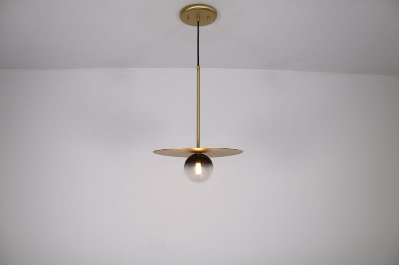 May include: A gold pendant light with a round, smoked glass shade and a flat, circular canopy.