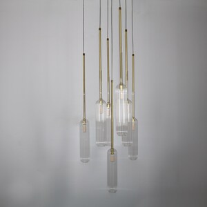 May include: A set of seven clear glass pendant lights with a ribbed texture, hanging from a white ceiling. Each light has a gold metal cord.