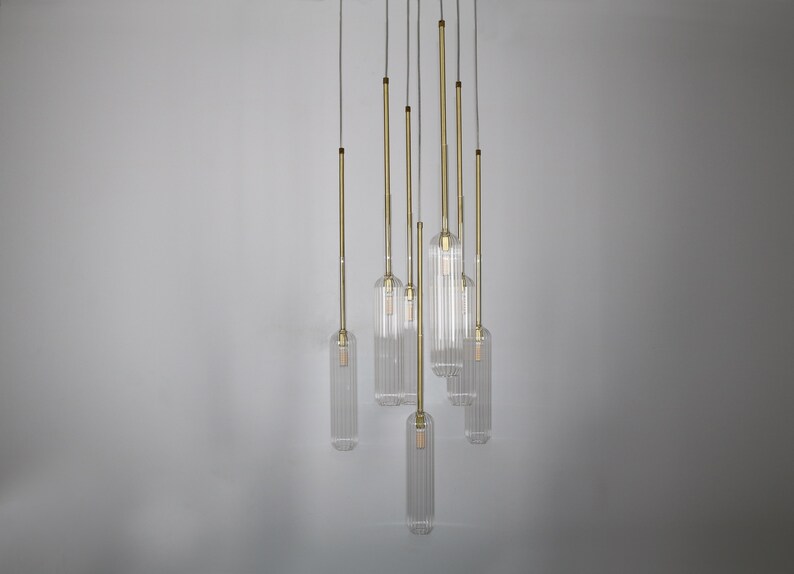 May include: A set of seven clear glass pendant lights with a ribbed texture, hanging from a white ceiling. Each light has a gold metal cord.