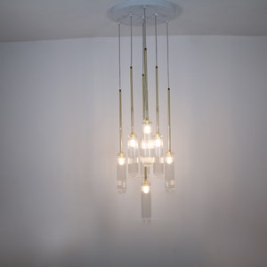 May include: A modern gold chandelier with clear glass cylinder shades. The chandelier has eight lights and is hanging from a white ceiling.