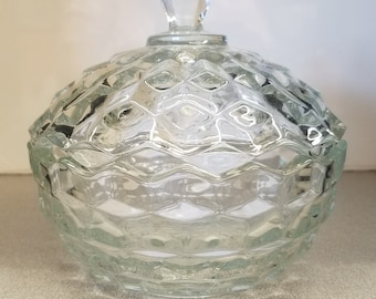 Pode incluir: Um prato de doces de vidro transparente com uma tampa abobadada. O prato tem um padrão de diamante e um botão no topo da tampa.
