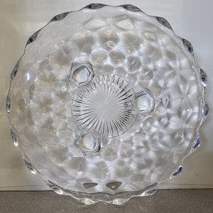 May include: A clear glass serving dish with a scalloped edge and a textured surface. The dish has three feet and a starburst pattern in the center.