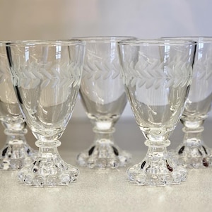 May include: Five clear glass wine glasses with a delicate etched leaf design on the bowl and a textured, bulbous base.