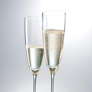 May include: Two champagne flutes filled with sparkling wine. The clear glasses have long stems and are partially filled with bubbly, light-colored liquid. The background is a soft, gradient white.