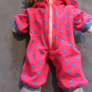 Könnte beinhalten: Ein rosa Kapuzen-Strampler mit blauen Sternen für eine Baby-Puppe. Der Strampler hat einen Reißverschluss an der Vorderseite.