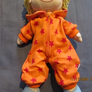 Könnte beinhalten: Orangefarbener Kapuzenoverall mit rosa Sternen für eine Puppe. Der Overall hat einen Reißverschluss an der Vorderseite.