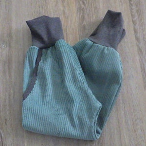Puede incluir: Un pantal&oacute;n de pana azul con pu&ntilde;os de canal&eacute; grises. El pantal&oacute;n est&aacute; doblado por la mitad y colocado plano sobre un suelo de madera.