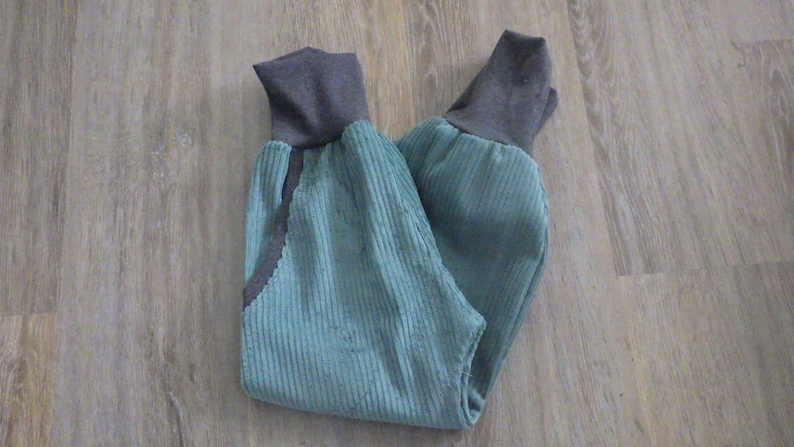 Puede incluir: Un pantal&oacute;n de pana azul con pu&ntilde;os de canal&eacute; grises. El pantal&oacute;n est&aacute; doblado por la mitad y colocado plano sobre un suelo de madera.