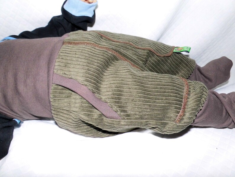 May include: A pair of green corduroy trousers with brown stitching. The trousers have a brown waistband and are turned up at the ankles.