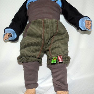 May include: A pair of green corduroy trousers with brown leggings underneath. The trousers have a brown waistband and red and green fabric accents.