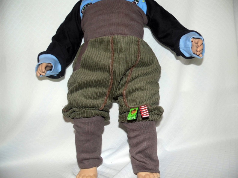 May include: A pair of green corduroy trousers with brown leggings underneath. The trousers have a brown waistband and red and green fabric accents.