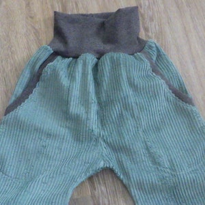 Puede incluir: Un pantal&oacute;n de pana azul verdoso con una cintura de canal&eacute; gris. El pantal&oacute;n tiene dos bolsillos grandes en la parte delantera.