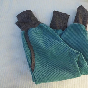 Puede incluir: Un pantal&oacute;n de pana azul turquesa con pu&ntilde;os de canal&eacute; grises. El pantal&oacute;n est&aacute; doblado por la mitad y tiene una costura en el lateral.