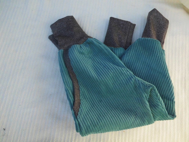 Puede incluir: Un pantal&oacute;n de pana azul turquesa con pu&ntilde;os de canal&eacute; grises. El pantal&oacute;n est&aacute; doblado por la mitad y tiene una costura en el lateral.