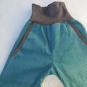 Puede incluir: Pantal&oacute;n de pana color turquesa con cintura el&aacute;stica gris oscuro y ribetes negros a los lados.