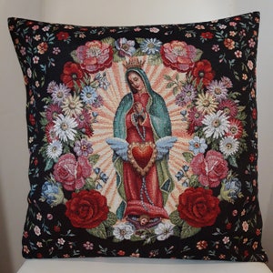 May include: A black cushion with a tapestry design featuring a depiction of the Virgin Mary with a heart and wings. The design is surrounded by colourful flowers and a black background with small white flowers.